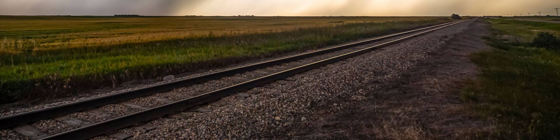 Dark storm clouds over railroad tracks in a field with rain falling in the distance; Marquis, Saskatchewan, Canada
