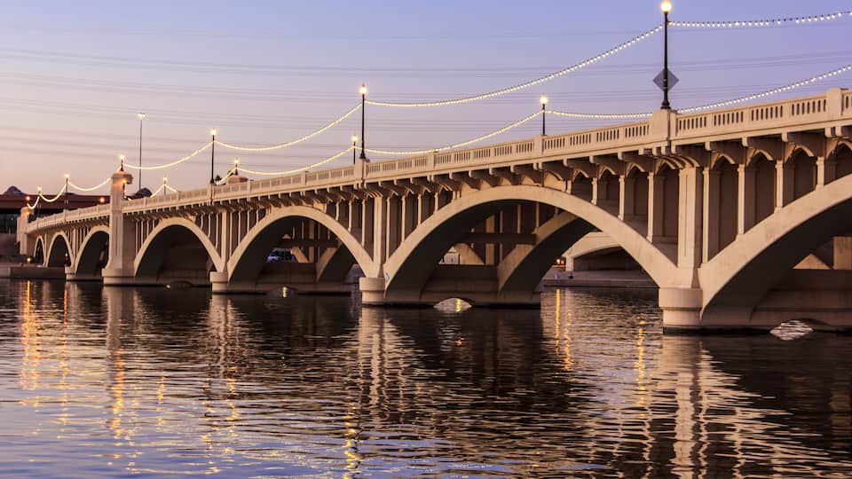 A bridge with multiple arches over a body of water, illuminated by string lights.