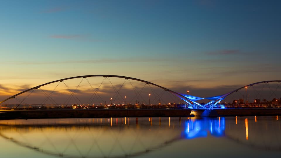 A bridge at dusk with its lights reflecting on the water.