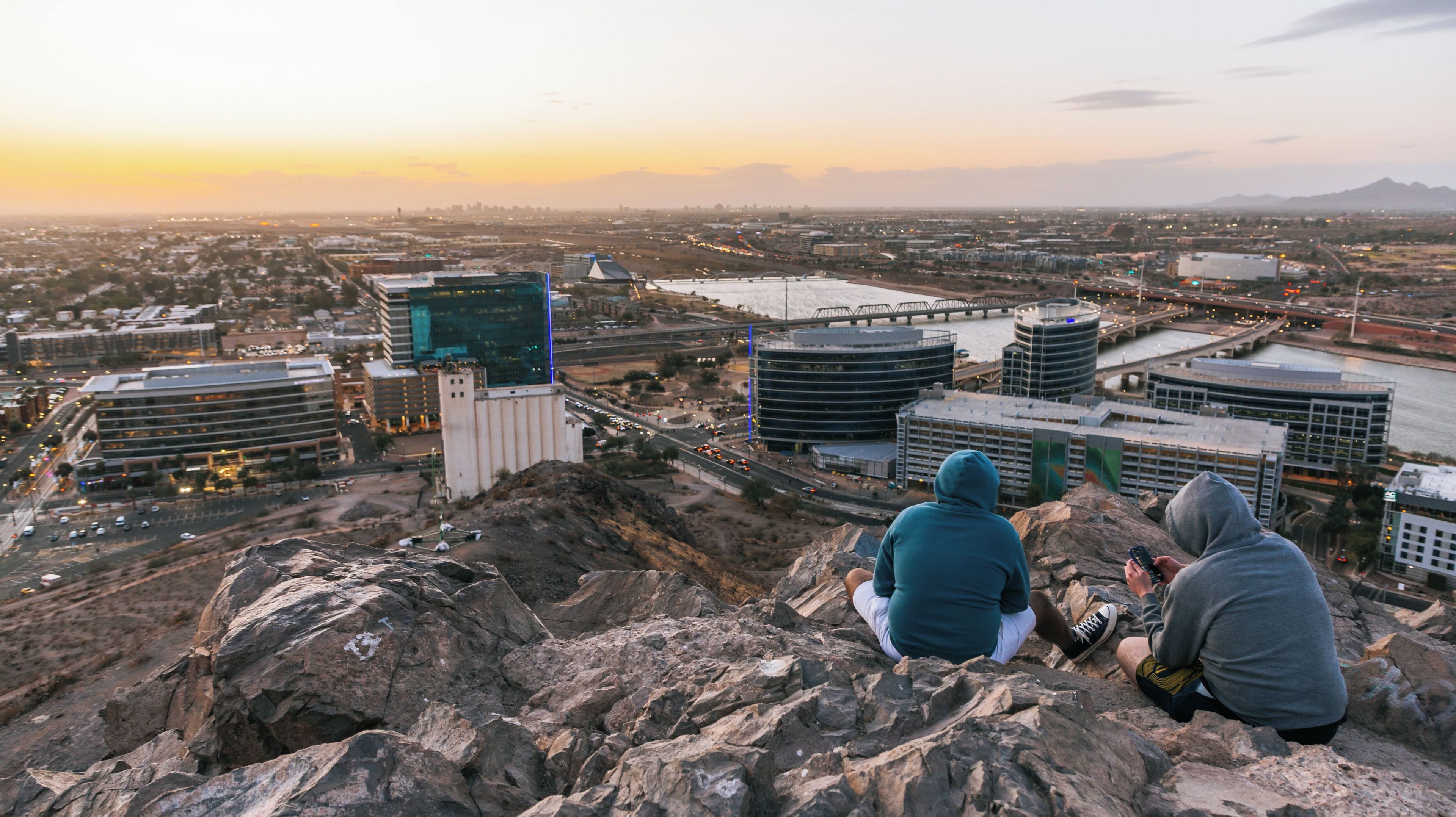 A cityscape with modern buildings, a bridge, and a rocky hill with two people sitting.