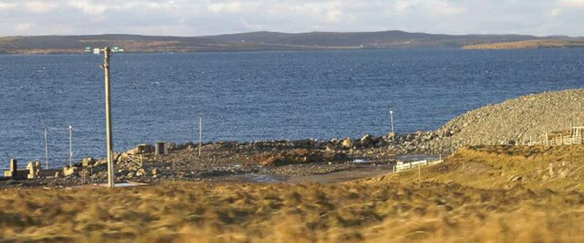 A coastal landscape with a rocky shoreline, a body of water, and distant hills.