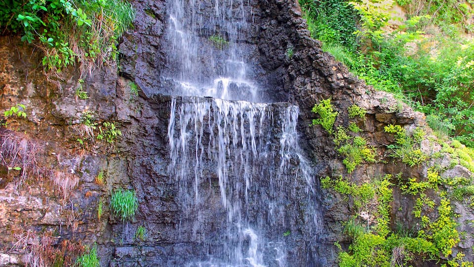 A multi-tiered waterfall cascading down a rocky cliff surrounded by lush greenery.