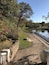 A park with a paved walkway, a bench, and a body of water.