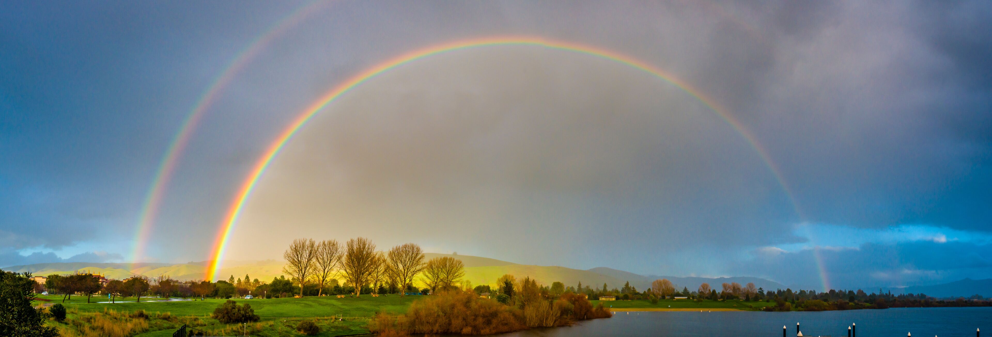 A landscape with a lake, trees, and a rainbow.