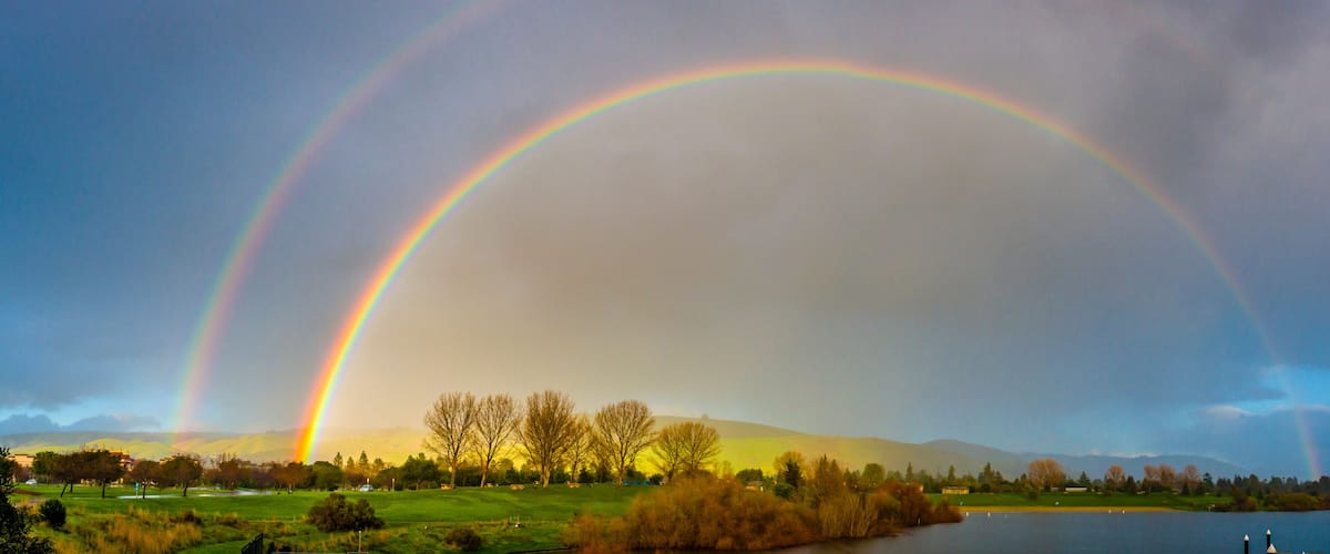 A landscape with a lake, trees, and a rainbow.