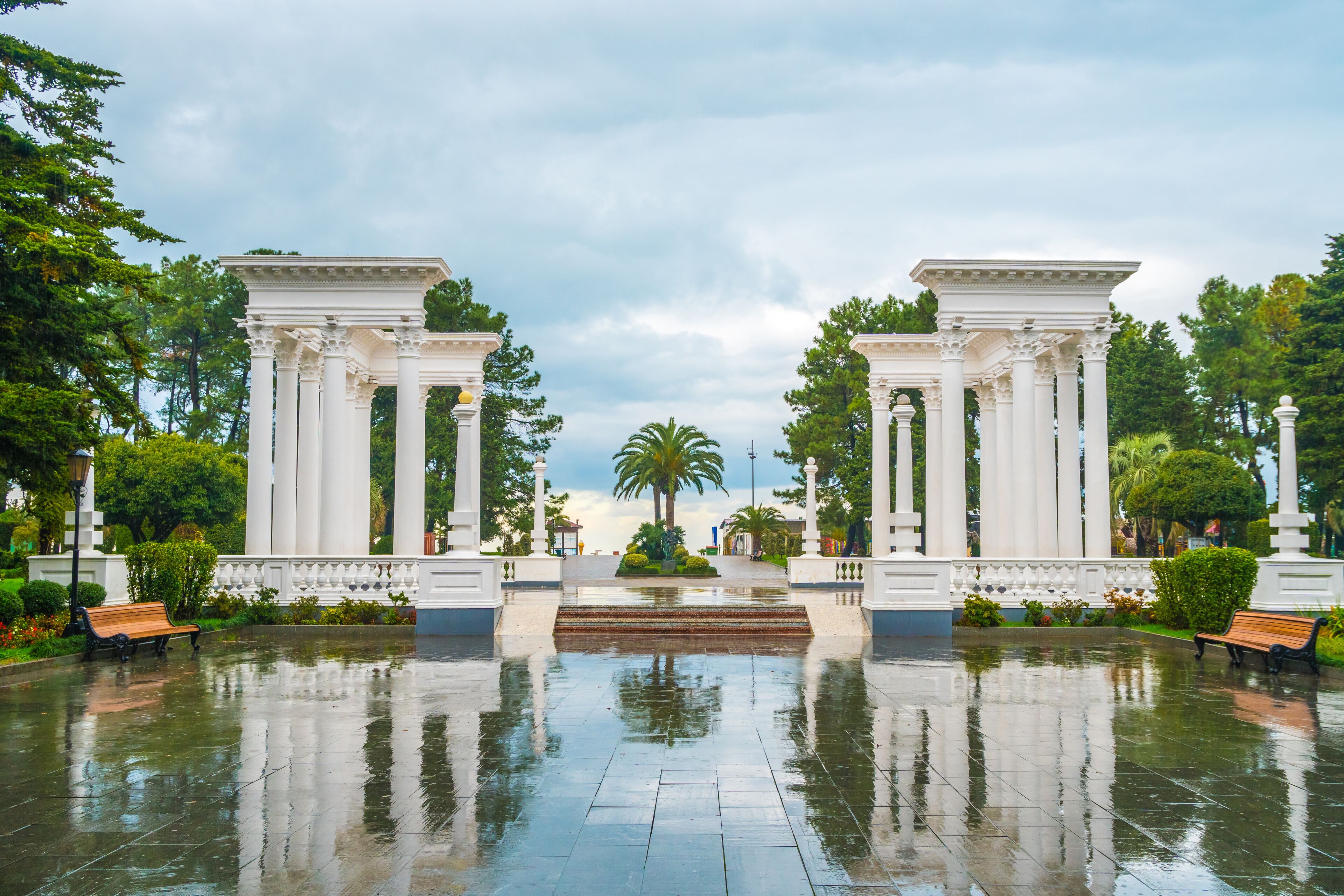 Una entrada clásica con columnas blancas, una palmera y un suelo brillante y húmedo.