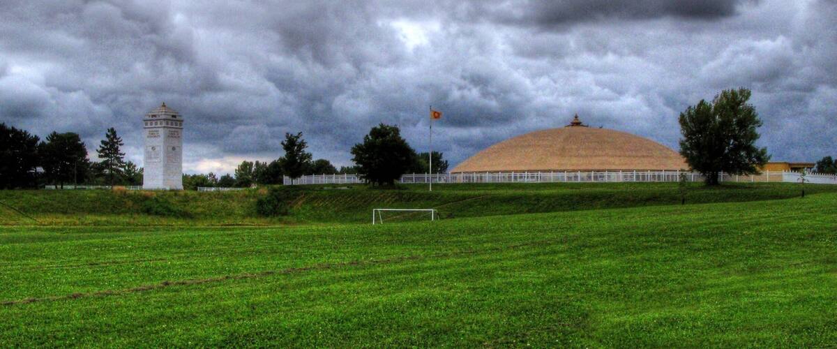 A green field with a white tower and a large dome building under a cloudy sky.