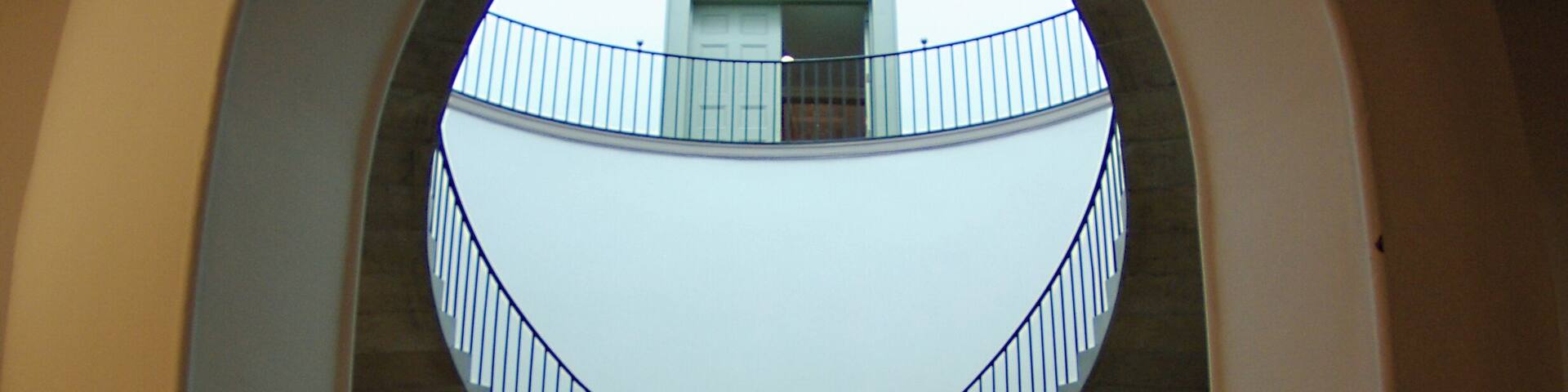 A grand staircase with a curved railing, leading to a balcony with a glass balustrade.
