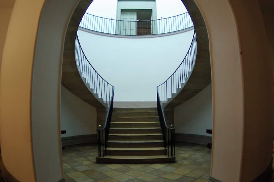 A grand staircase with a curved railing, leading to a balcony with a glass balustrade.