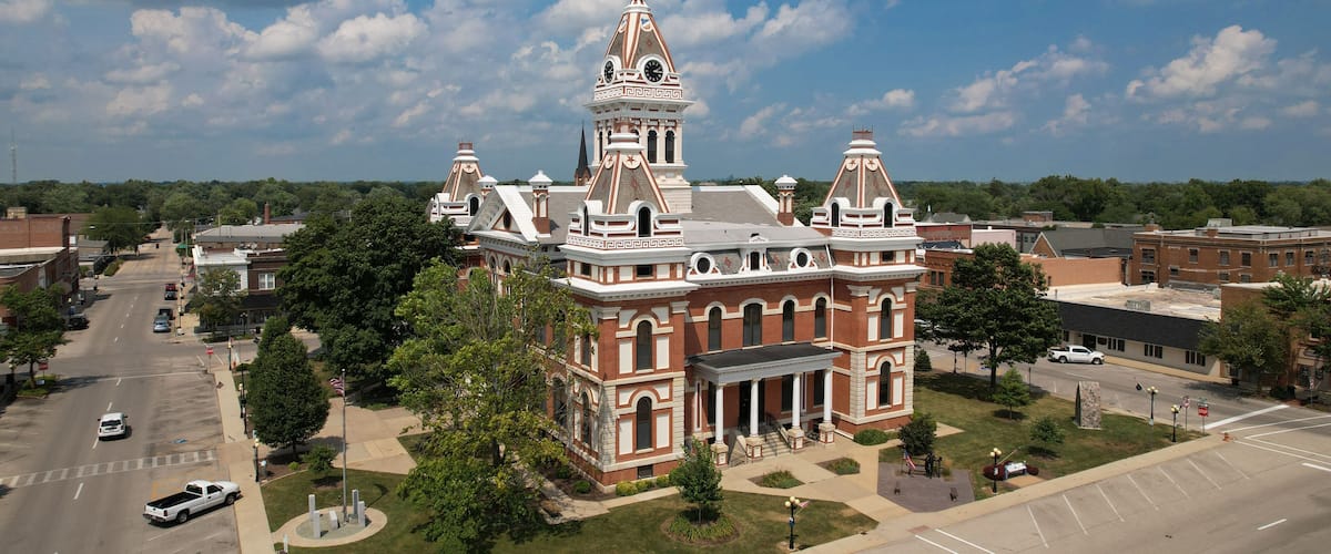 A large, historic building with a prominent tower and columns, surrounded by a parking lot and a street.