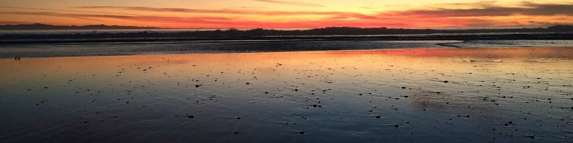 Un atardecer sobre una playa tranquila con superficie acuática reflectante.