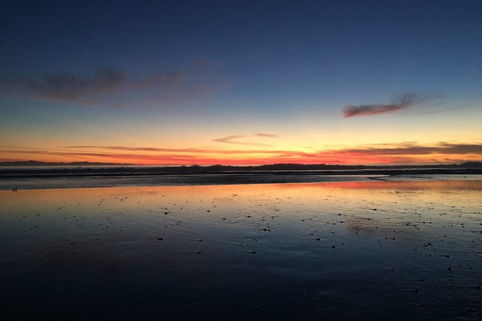 A sunset over a calm beach with a reflective water surface.