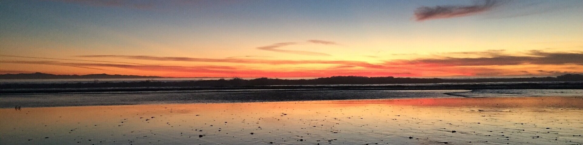 Un atardecer sobre una playa tranquila con superficie acuática reflectante.