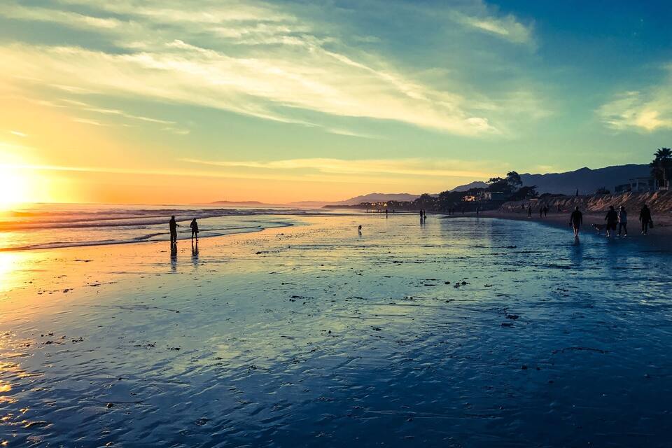 A beach at sunset with people walking along the shore.