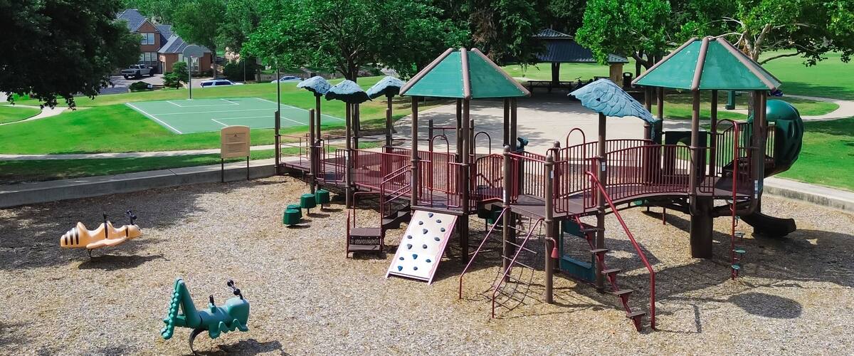 A playground with climbing structures, a slide, and a basketball court in the background.