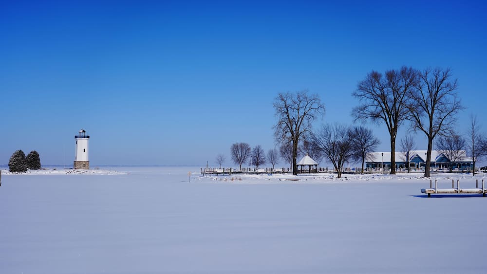 A snow-covered landscape with a lighthouse, trees, and a building.