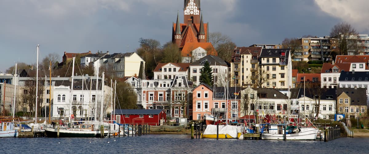 A harbor with boats, a church with a tall spire, and residential buildings.