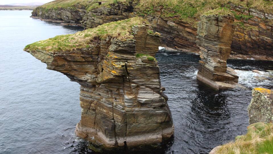 A coastal rock formation with layered cliffs and a narrow water passage.