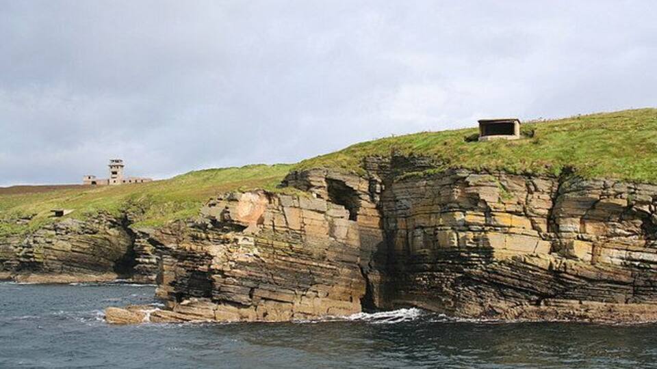 A coastal cliff with layered rock formations and a lighthouse in the background.