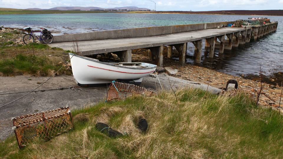 A small boat tied to a concrete pier by a grassy shore.