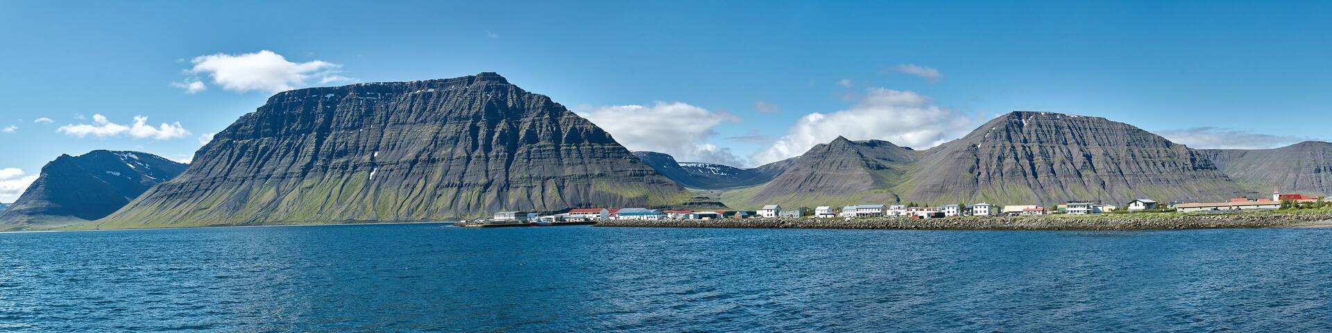 Travel to Iceland. beautiful sunrise over the ocean and fjord in Iceland. Icelandic landscape with mountains, blue sky and green grass on the foreground. View of Flateyri, a village in the north-west