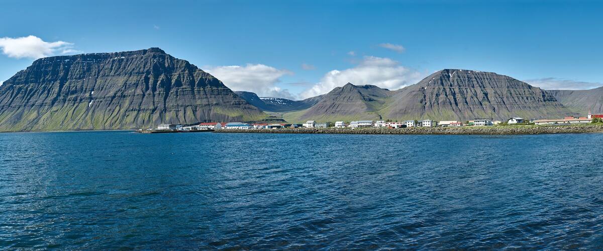 A coastal town with houses along the shore, a fjord, and mountains in the background.