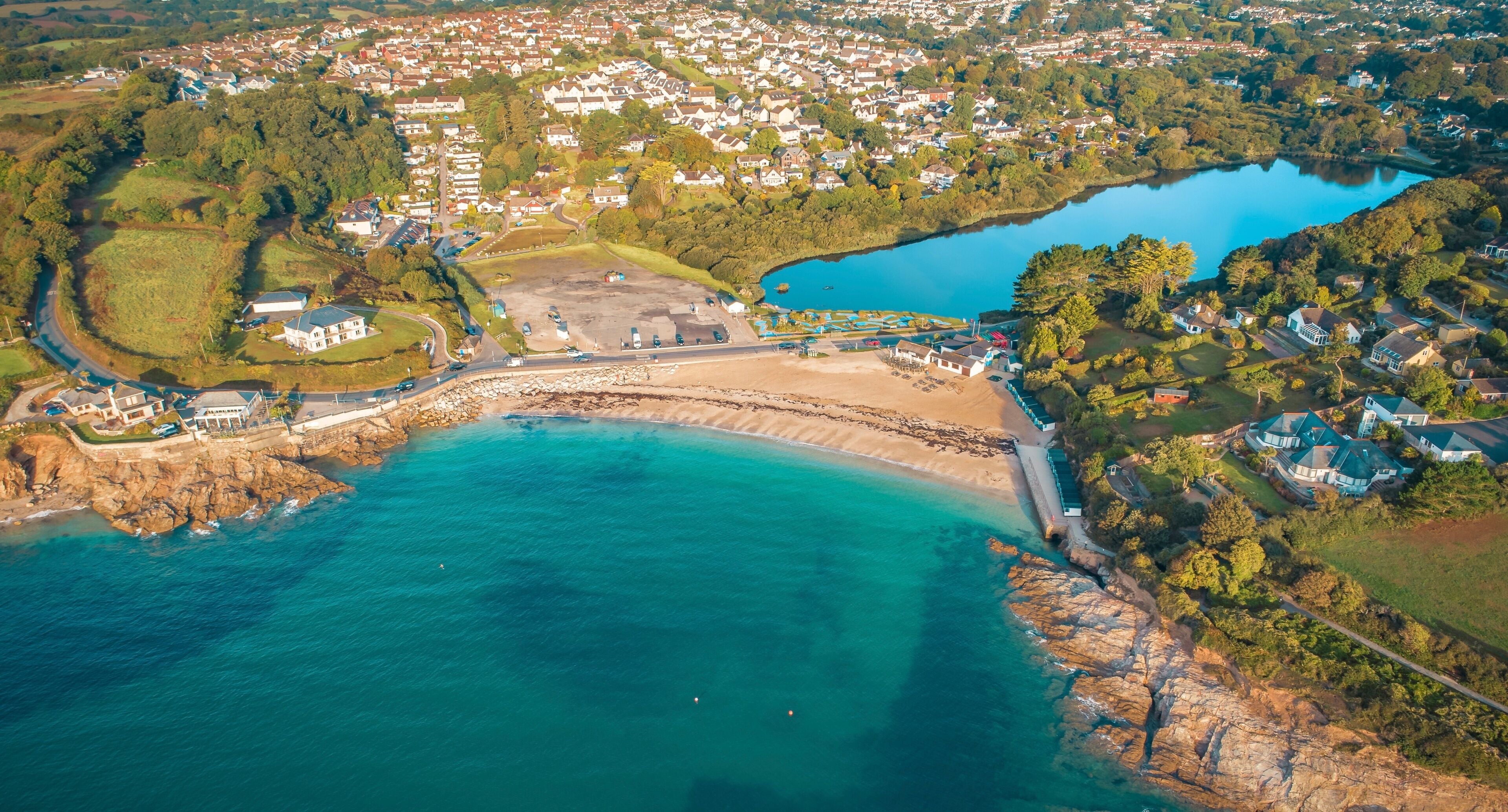 An aerial view of a coastal town with a beach, a large lake, and residential areas.