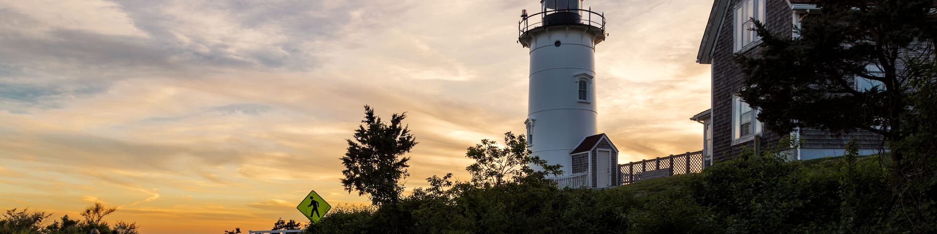 A road curving past a white lighthouse and a house with a red roof.