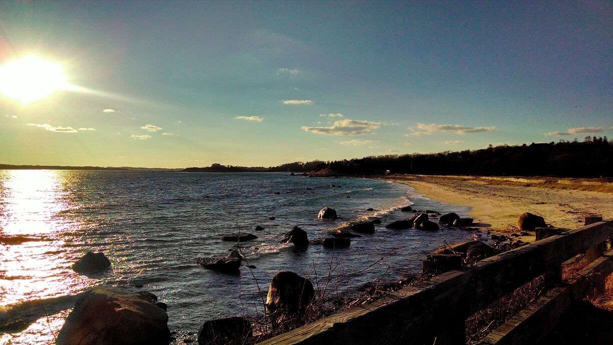 A beach with rocks in the water, a sandy shore, and a clear sky.