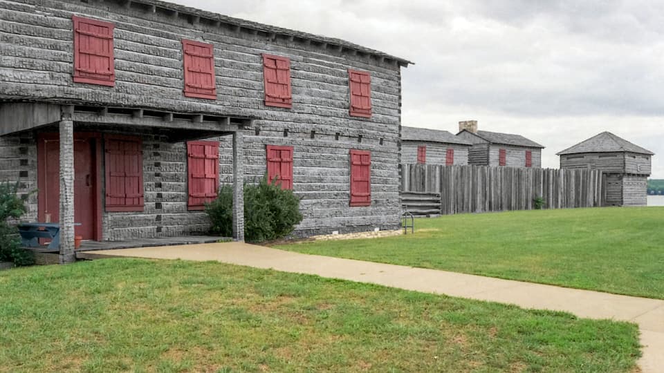 A rustic wooden building with red shutters and a wooden fence.