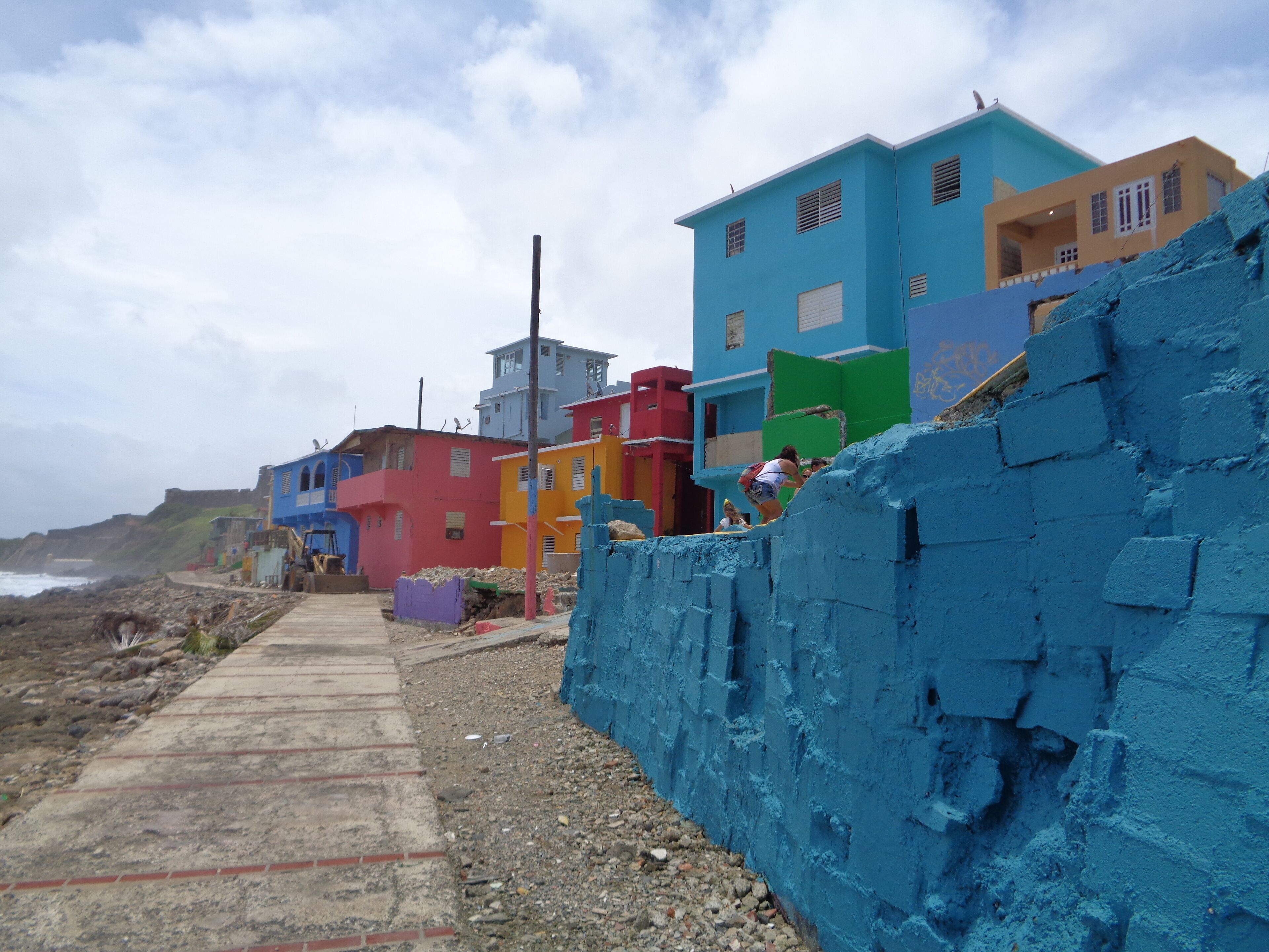 A coastal street lined with colorful houses, a concrete path, and a rocky shoreline.