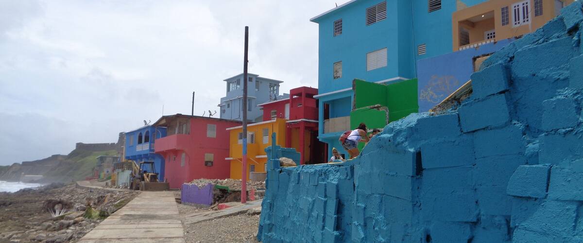 A coastal street lined with colorful houses, a concrete path, and a rocky shoreline.