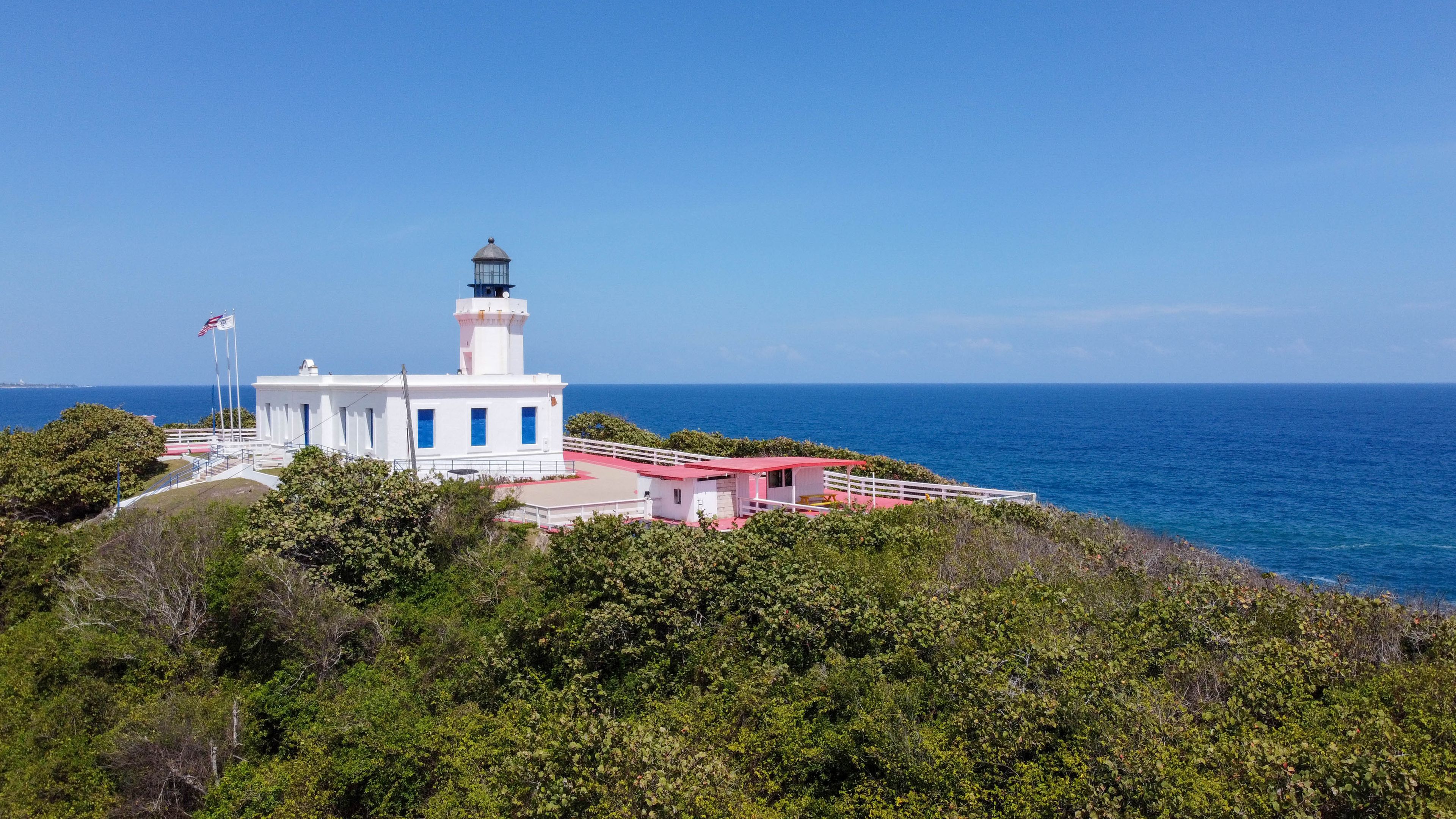 Un faro con estructura blanca y azul, rodeado de exuberante vegetación y el océano.