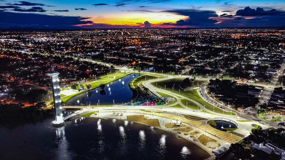 Un paisaje urbano al atardecer con un parque costero destacado y un monumento alto.