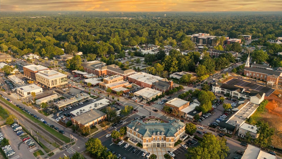 An aerial view of a town with a central building surrounded by streets and parked cars.