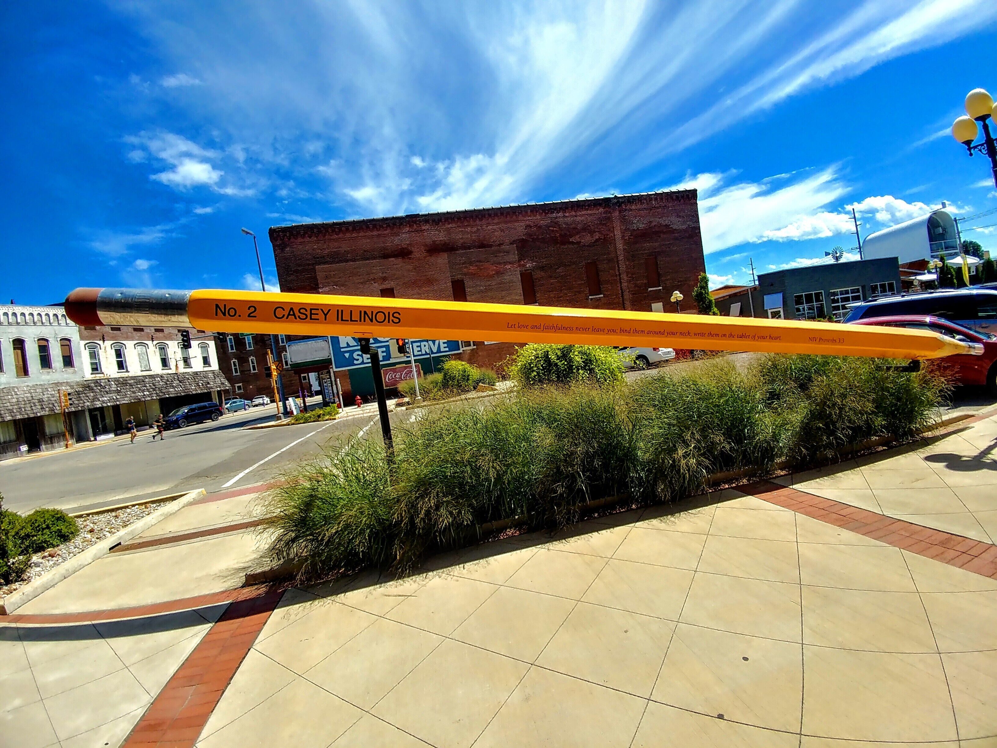 A street with a large pencil sculpture, a brick building, and a Coca-Cola sign.