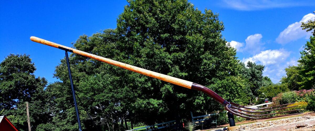 A baseball bat leaning against a fence in a park with trees and a clear sky.