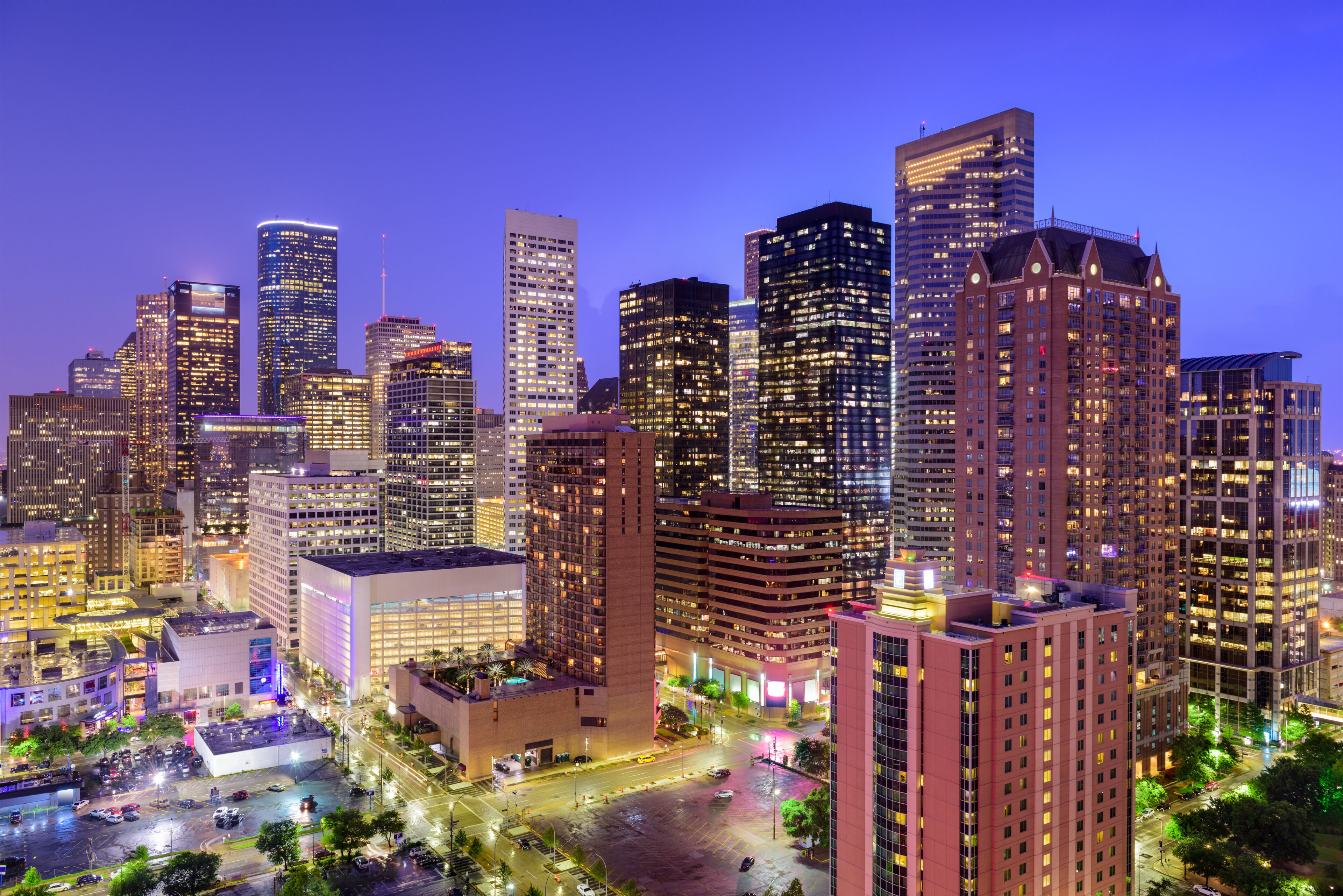 A cityscape at dusk with illuminated skyscrapers and a busy intersection.