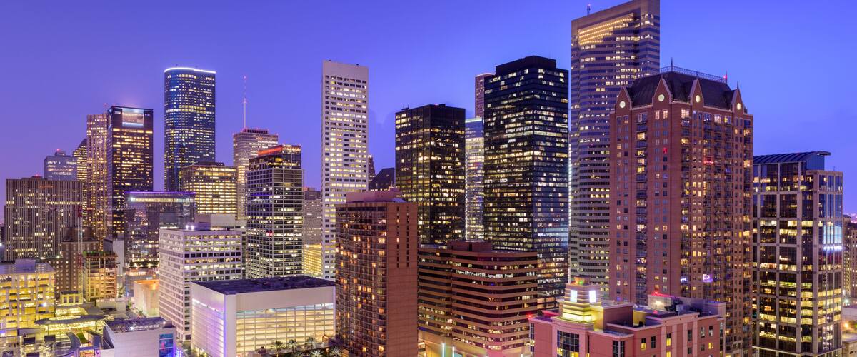 A cityscape at dusk with illuminated skyscrapers and a busy intersection.