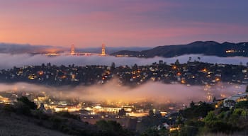 A coastal town at sunset with a bridge in the background and fog over the water.