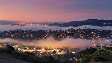 Un pueblo costero al atardecer con un puente al fondo y niebla sobre el agua.