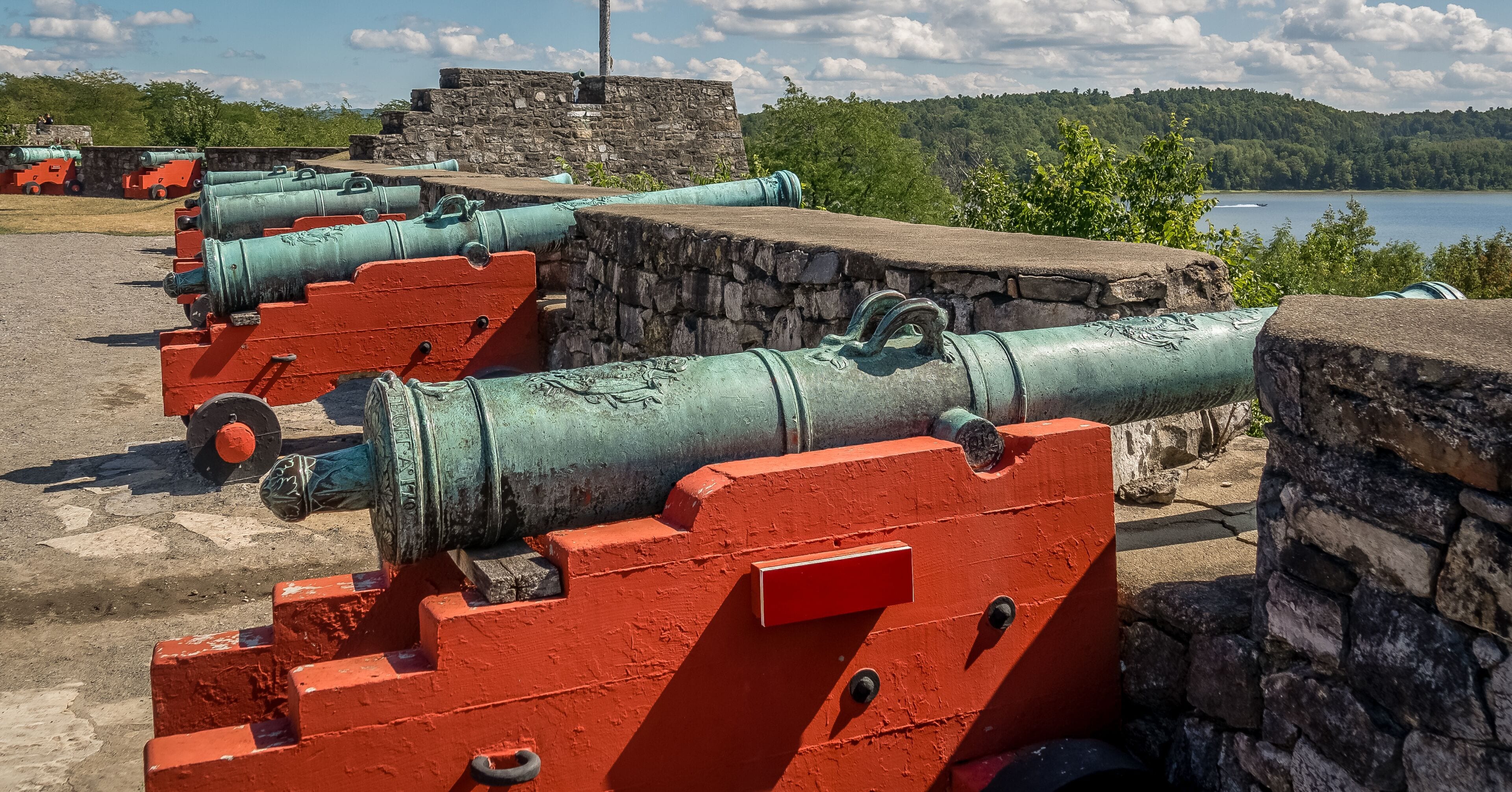 Row of 18th century bronze cannons with red base in firing position over Lake George with American flag