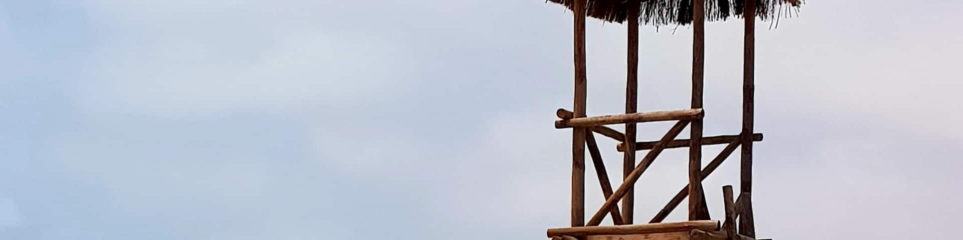 A wooden lifeguard tower on a beach with turquoise water and a clear sky.