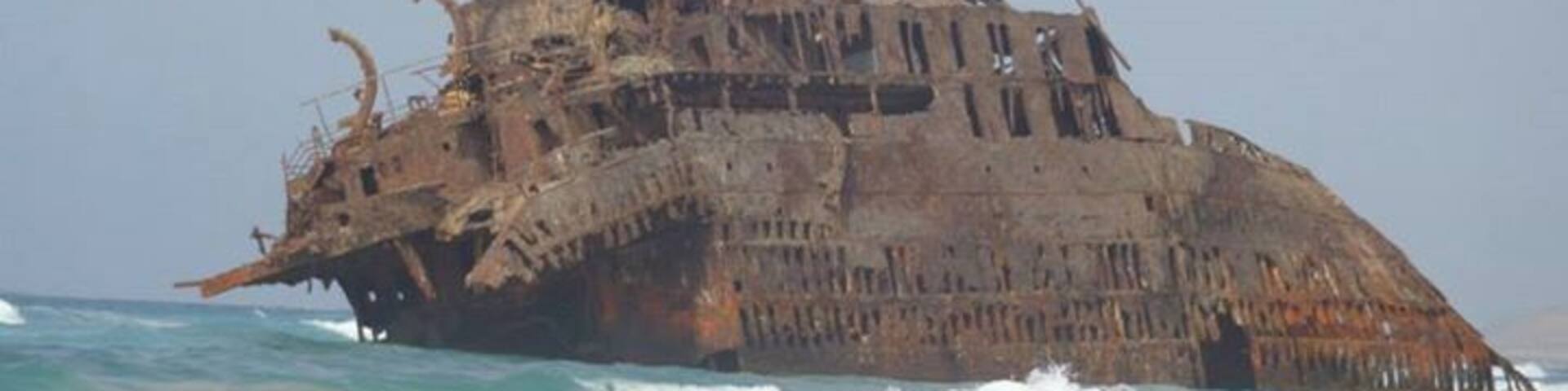 A large, rusted shipwreck in the ocean.