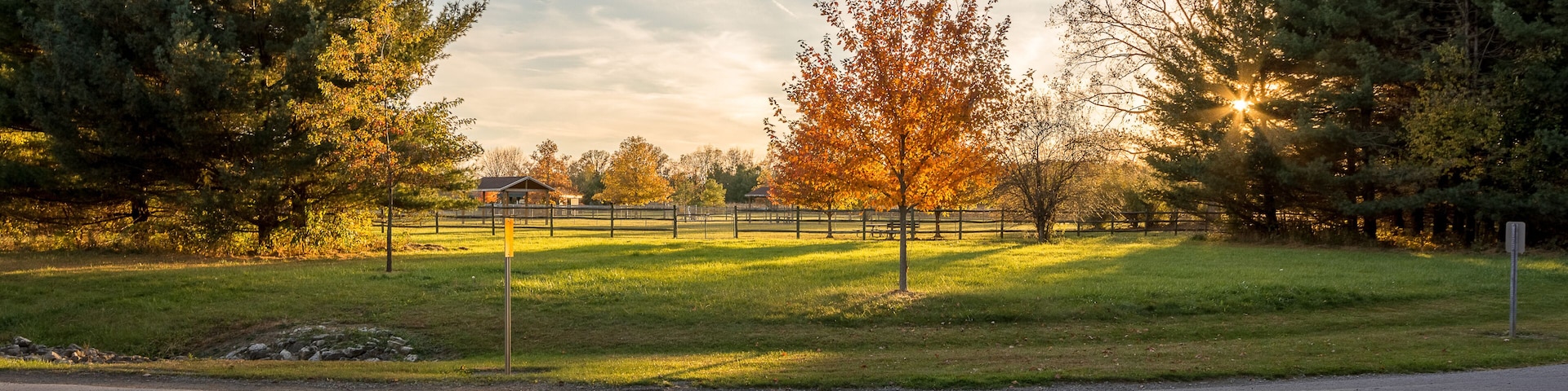 A park with a paved path, trees, and a fence.