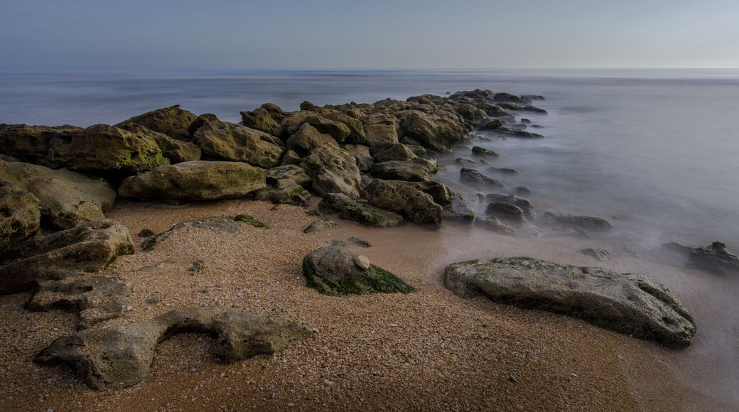 A rocky shoreline with a calm sea and clear sky.