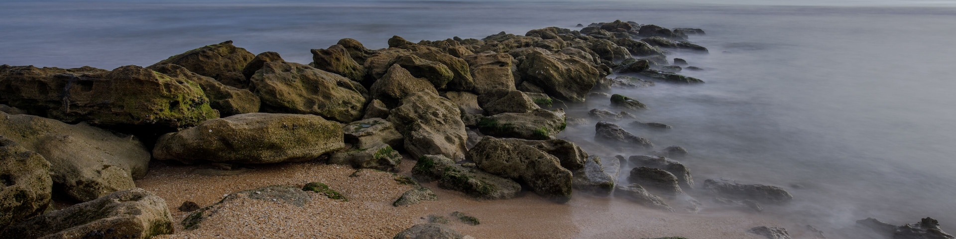 Uma costa rochosa com mar calmo e céu claro.