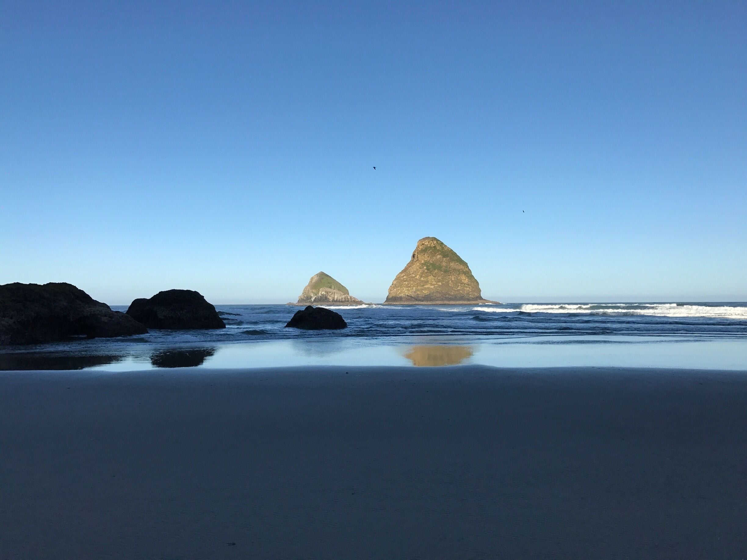 A beach with two prominent rock formations in the distance under a clear blue sky.