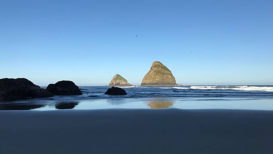A beach with two prominent rock formations in the distance under a clear blue sky.