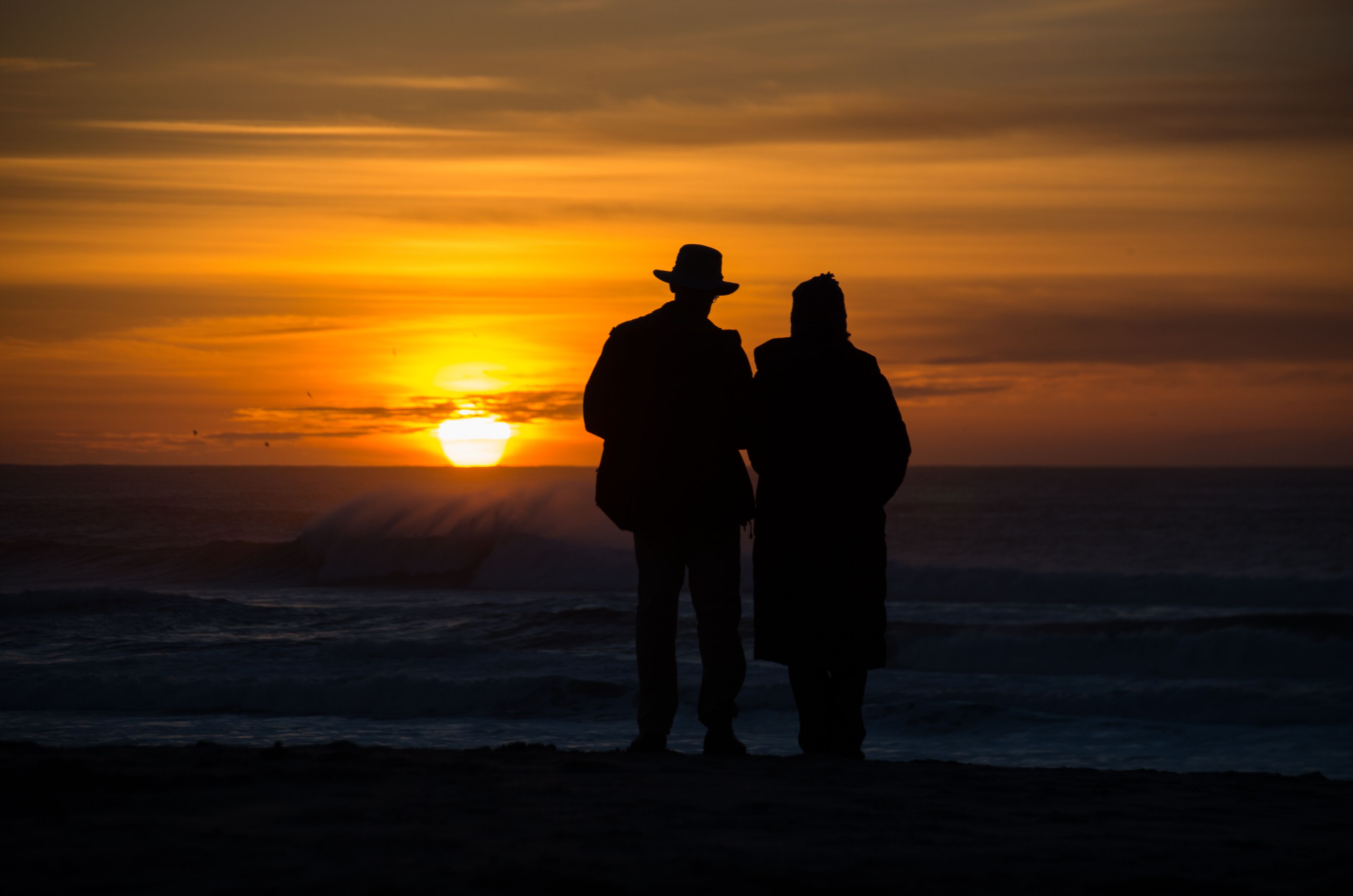 Silueta de dos personas de pie en la playa durante la puesta de sol.